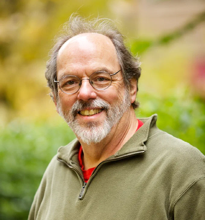 Portræt af Ward Cunningham, som opfandt wiki’en, smilende med briller og gråt skæg og en grøn trøje foran en uskarp have